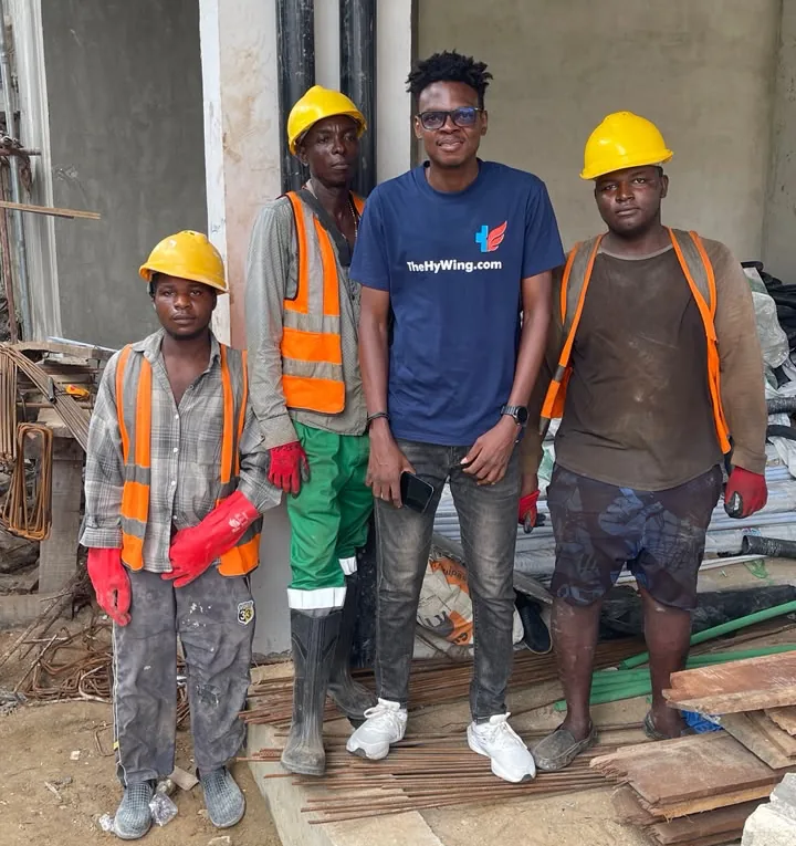 A person wearing a TheHyWing T-shirt standing with three construction workers at a building site.
